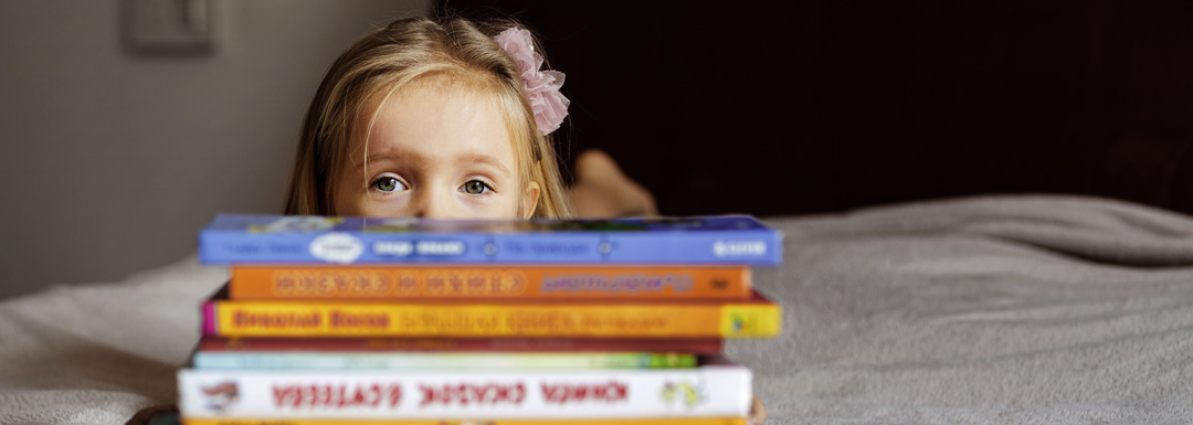 Kleines Mädchen hinter einem Stapel voller Kinderbücher