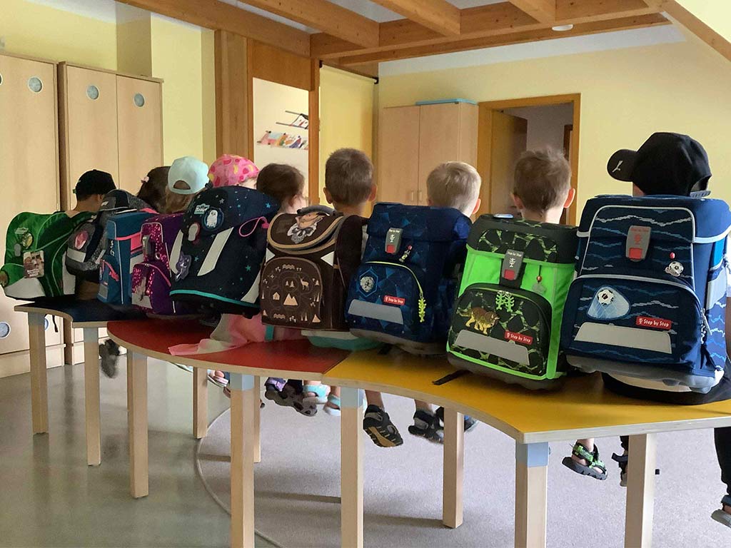 Kindergartenkinder sitzen auf Tischen und präsentieren ihre zukünftigen Schulranzen